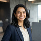A friendly South Asian woman smiling in a professional headshot, set against a modern, minimalist charcoal and white backgrou